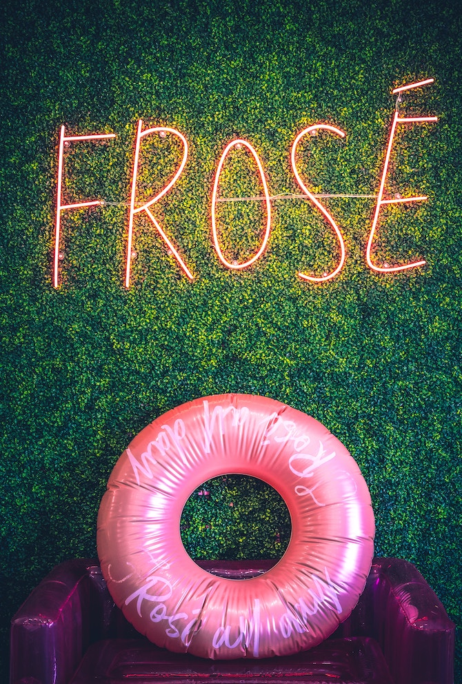 A green faux plant wall with a "frose" neon sign and a pink innertube