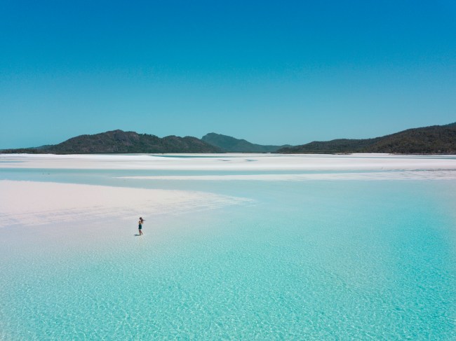 Girl walking on Whitehaven Beach in shallow water (Queensland, Australia).
Drone shot from above. White sand and blue water.