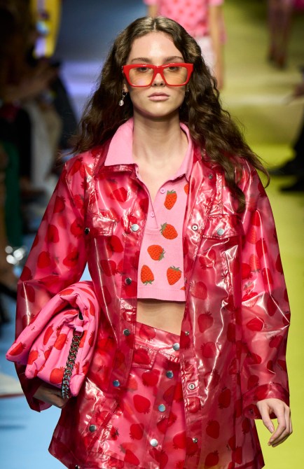 A runway model wears a pink and red strawberry outfit with oversized, red glasses.