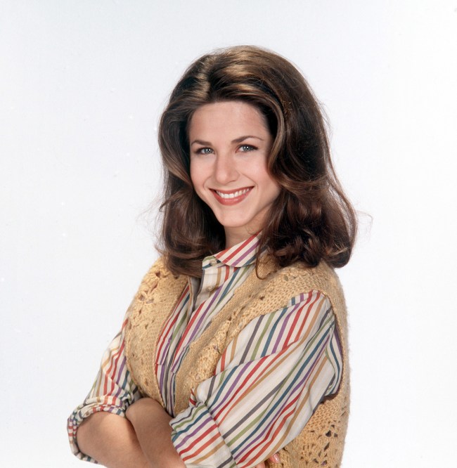 Jennifer Aniston as Madeline Drego Cooper in a rainbow striped shirt and knit vest with shoulder length dark brown hair