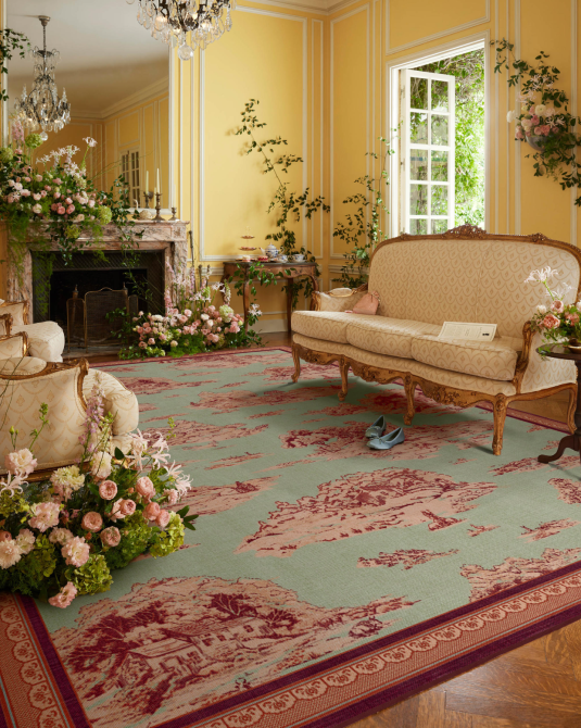 A yellow living room with Regency-era furniture, floral arrangements, and a large blue and pink printed rug