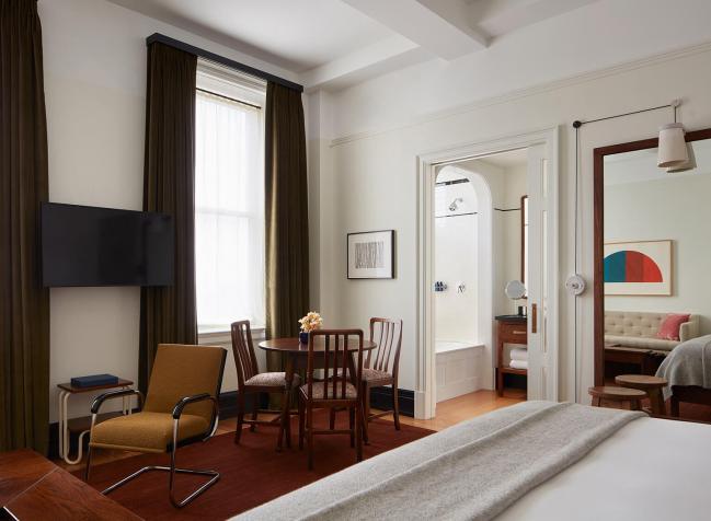 A bedroom at the Nine Orchard Hotel, which features a bed, dining nook, desk, and doorway leading to additional living space