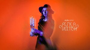 A witch woman holding a candelabra in purple tones, standing in front of an orange background, getting ready to give someone life-saving advice using astrology.