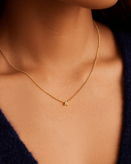 A model wearing the Gorjana Wilder Mini Alphabet Necklace in gold and with the letter A