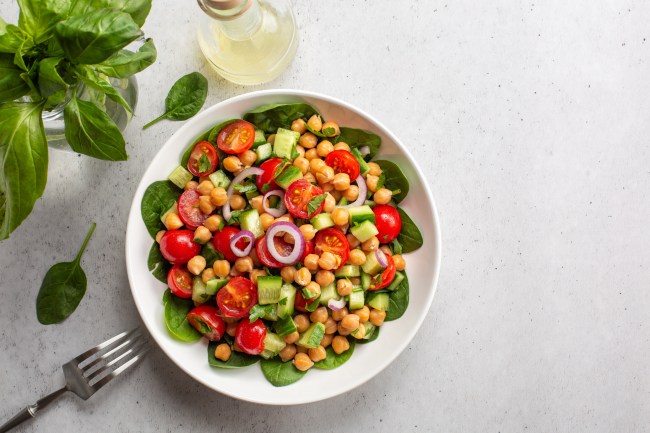 Fresh summer mediterranean salad with chickpea, tomatoes, cucumbers, spinach, red onion, parsley.