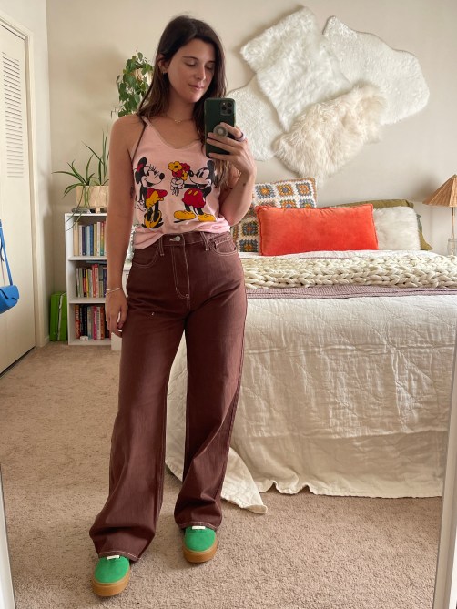 A woman in a pink tank with Minnie and Mickey on it, brown jeans, and green sneakers