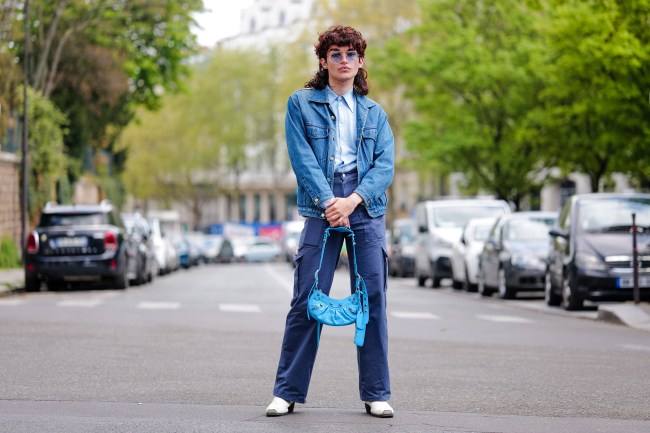 Loic Hornecker wears navy blue circle sunglasses, a pale blue shirt, a navy blue denim jacket in Paris, France.