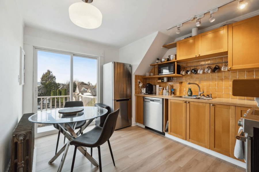 A kitchen with wood cabinets and stainless steel kitchen appliances, and a dining table with two chairs. A Kitsilano, Vancouver Airbnb.