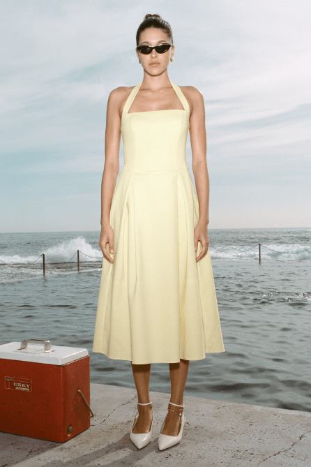 A model wearing Meshki Juana Halter Midi Dress in. butter yellow colorway