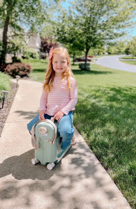 A little girl sitting on top of Stokke's Kids' BedBox® 19-Inch Ride-On Carry-On Suitcase